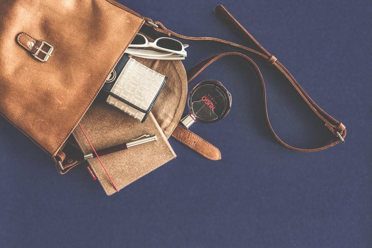 Stylish flat lay of a leather handbag with luxury accessories including sunglasses, wallet, notebook, and pen.